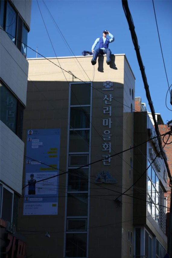 부산 중구 영주동 산리마을회관 옥상에 마을지기사무소에서 근무하는 만물수리공의 실제 모습을 본떠 만든 조형물이 설치돼 있다.