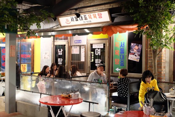 포차어게인은 테이블 위의 처마에서 물줄기가 흘러내리도록 해 비 오는 날 야외 포장마차에서 술을 즐기는 낭만을 느낄 수 있도록 연출했다. 서울 역삼동 포차어게인 강남본점에서 손님들이 낭만을 즐기며 음식을 즐기고 있다.