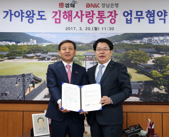 손교덕 경남은행장(오른쪽)과 허성곤 김해시장이 20일 ‘가야왕도 김해사랑통장' 업무협약서를 들고 기념촬영을 위해 포즈를 취하고 있다.