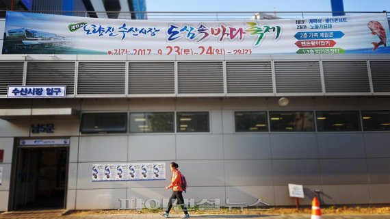 ▲ 지난 주말 노량진 수산시장에서 열린 '도심 속 바다축제' 현수막 아래로 한 중년 여성이 지나가고 있다./사진=정용부 기자