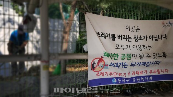 ▲ 서울시 동작구 수산시장 지하도 입구에 붙여진 쓰레기 무단투기 금지 현수막 뒤로 직원이 환경정비를 하고 있다.