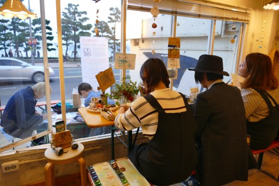 부산 광안리의 보물섬이란 별칭을 달고 있는 마을기업 '오랜지바다' 매장에서 고객들이 그림엽서 작업을 하고 있다.