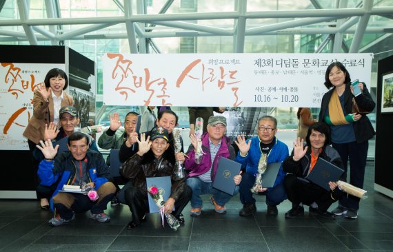 현대엔지니어링이 서울 쪽방촌 주민과 함께한 '디딤돌 문화교실'의 작품을 16~20일 세종대로 서울시청에서 전시한다. 18일 전시회 참가자들이 기념촬영을 하고 있다.