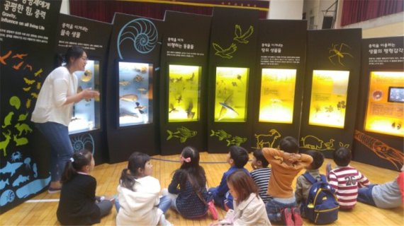 한국과학창의재단이 '두드림 프로젝트'로 진행하는 '찾아가는 과학관'은 전국을 순회하며 다양한 과학원리를 설명하고 체험할 수 있도록 한다. 찾아가는 과학관을 찾은 어린이들의 중력에 대한 설명을 듣고 있다.