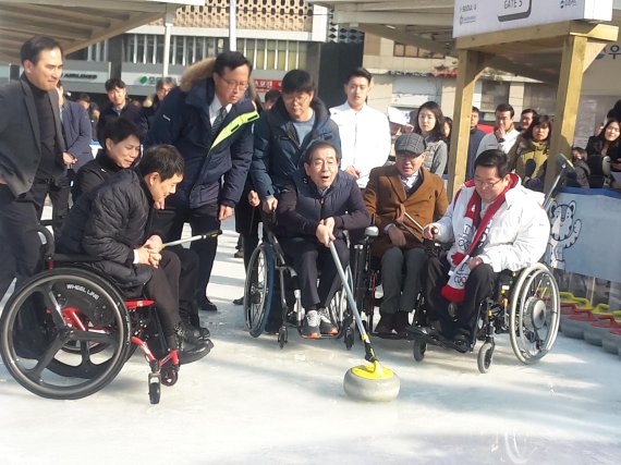 서울시가 26일 평창동계올림픽에 이어 패럴림픽에도 붐업 조성에 들어갔다. 박원순 서울시장은 이날 '2018 평창 패럴림픽 붐업 페스티발을 열고 이자리에서 장애인과 비장애인으로 나눠 컬링 경기를 벌였다. 박시장이 서울광장 스케이트장에서 휠체어를 타고 컬링 초구 스톤을 던지고 있다.