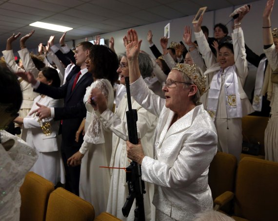 (뉴파운드랜드<美펜실베이니아주> AP=연합뉴스) 지난달 28일(현지시간) 미국 펜실베이니아주 뉴파운드랜드에 있는 '세계평화·통일 생추어리' 교회에서 열린 합동결혼 축복 예배에 한 여성 신도(앞줄 오른쪽)가 왕관을 쓴 채 총알이 없는 빈 자동소총을 들고 참석해 논란을 일으켰다.