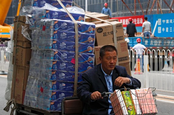 A man rides an electric bike loaded with boxes of tissue paper past by a construction site in Beijing, Wednesday, Sept. 19, 2018. China's No. 2 leader appealed Wednesday for support for free trade and promised to improve conditions for foreign companies following tit-for-tat U.S. and Chinese tariff 