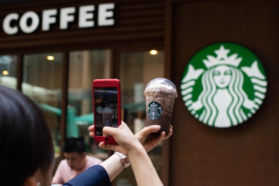 (FILES) This file picture taken on May 25, 2018 shows a woman taking a picture of her beverage at a Starbucks coffee shop in Beijing. Starbucks on August 2, 2018 announced a partnership with Alibaba that will see the US coffee chain utilise the Chinese ecommerce giant's logistics networks to tap dee
