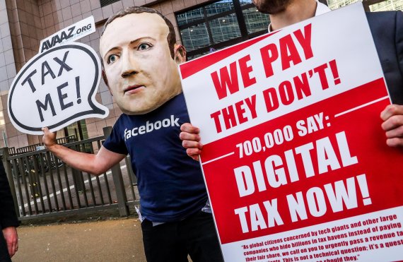 An activist wearing a mask depicting Facebook's CEO Mark Zuckerberg holds a banner reading 'Tax me' at the start of an European Union Finance Ministers Meeting in front of the European Council in Brussels, Belgium, 04 December 2018. Activists ask for an EU tax on big digital firms. EPA/STEPHANIE LEC