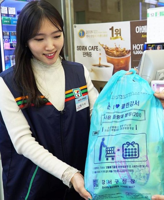 편의점 세븐일레븐은 서울 강서구와 손잡고 업계 최초로 손잡이가 달려서 장바구니로도 사용이 가능한 '재사용종량제봉투' 시범 판매에 나선다고 24일 밝혔다. 한 고객이 구매한 물건이 담긴 재사용종량제봉투를 건네 받고 있다. 세븐일레븐 제공