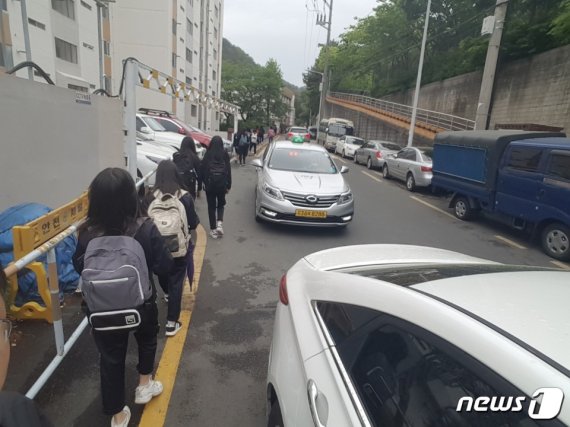 반송여중 학생들의 등굣길. 인도가 없어 주차된 차량들에 진출입 차량들까지 뒤엉켜 위험한 상황에 노출돼 있다.2019.06.12(반송여중 대책위 제공)© 뉴스1