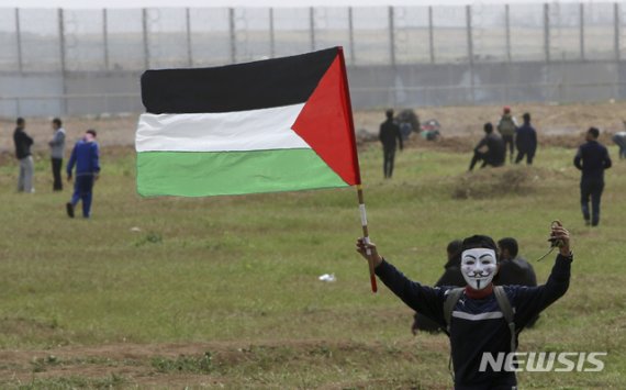 【가자=AP/뉴시스】이스라엘과 가자지구 국경지대에서 30일(현지시간) 가면을 쓴 한 시위자가 팔레스타인 국기를 흔들고 있다. 가자지구 봉쇄 해제를 요구하는 이날 시위에는 팔레스타인 시민 약 3만명이 참가했다. 2019.03.31.