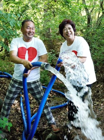 경남 김해시 진례면 산본리 산본마을에서 김정옥 산본마을 이장(왼쪽)과 김수진 관동마을 이장이 '맑은 도랑 살리기 2호 저수지'에서 흘러가는 수급 호스를 잡고 함박 웃음을 짓고 있다. 코카콜라 제공