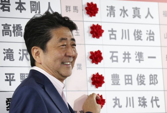 아베 신조 일본 총리가 지난해 7월 참의원 선거에서 승리한 후 밝은 표정으로 당선자 이름 앞에 붉은색 꽃을 달아주고 있다. AP뉴시스