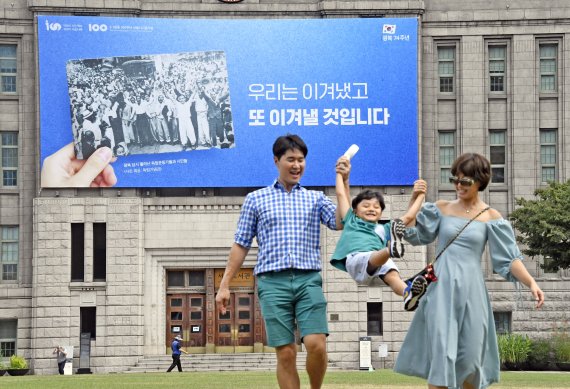 11일 서울 중구 서울도서관 외벽에는 광복 제74주년을 맞이해 광복 당시 풀려난 독립운동가와 시민들 사진과 함께 '우리는 이겨냈고, 또 이겨낼 것입니다'라는 문구의 꿈새김판이 걸려 있다. 이번 꿈새김판에는 74년 전 민족의 염원으로 독립을 이뤄낸 것처럼 시민 모두가 화합해 현 시대의 난관을 극복하고자 하는 염원이 담겼다. 나들이를 나온 한 가족이 서울광장 앞을 지나가고 있다. 사진=박범준 기자