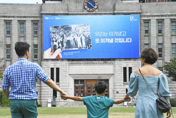 11일 서울 중구 서울도서관 외벽에는 광복 제74주년을 맞이해 광복 당시 풀려난 독립운동가와 시민들 사진과 함께 '우리는 이겨냈고, 또 이겨낼 것입니다'라는 문구의 꿈새김판이 걸려 있다. 이번 꿈새김판에는 74년 전 민족의 염원으로 독립을 이뤄낸 것처럼 시민 모두가 화합해 현 시대의 난관을 극복하고자 하는 염원이 담겼다. 나들이를 나온 한 가족이 서울광장 앞을 지나가고 있다. 사진=박범준 기자