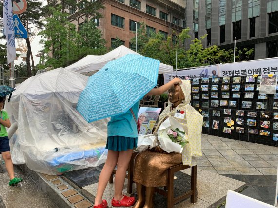 15일 서울 종로구 옛 일본대사관 앞에서 평화의 소녀상을 찾은 시민이 시민이 우비를 입은 소녀상을 쓰다듬고 있다./사진=강현수 인턴기자