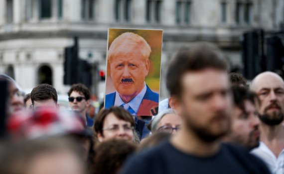 영국 런던의 총리관저 밖에서 28일(현지시간) 시위대가 보리스 존슨 영국 총리의 얼굴에 아돌프 히틀러를 연상하게 하는 콧수염을 그려넣은 사진을 들고 행진하고 있다.로이터뉴스1