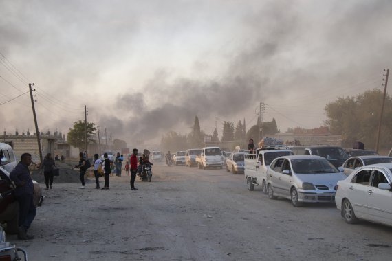 시리아 북부 국경도시인 라스 알 아인에서 9일(현지시간) 터키군의 공격에 연기가 피어오르는 가운데 남쪽으로 향하는 피난민들의 차량이 도로를 메우고 있다.AP뉴시스
