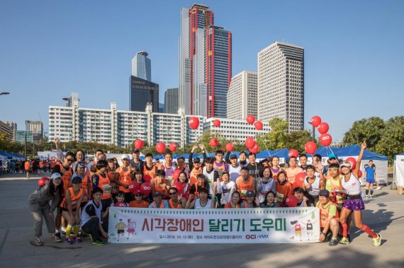 OCI직원들이 창립 60주년을 맞아 지난 12일 서울 여의도한강공원에서 열린 시각장애인 마라톤 대회에서 참가들과 단체사진을 찍고 있다.