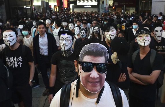 A man wearing a mask of Chinese President Xi Jinping stands with peole wearing Guy Fawkes masks on a street in Hong Kong, Thursday, Oct. 31, 2019. Hong Kong authorities are bracing as pro-democracy protesters urged people on Thursday to celebrate Halloween by wearing masks on a march in defiance of 