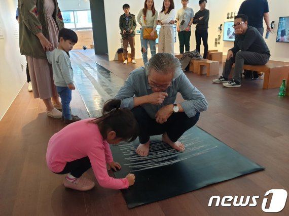 지난 10월24일 헬로우뮤지움에서 이건용 작가가 '달팽이 걸음' 퍼포먼스를 펼친 뒤 자신을 응원해준 어린이를 위해 작품에 이름을 적게 하는 모습.© 뉴스1 이기림 기자