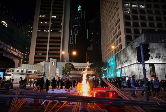Demonstrators gather near a burning barricade in the street during a protest in Hong Kong, Saturday, Nov. 2, 2019. Anti-government protesters attacked the Hong Kong office of China's official Xinhua News Agency for the first time Saturday after chaos broke out downtown, with police and demonstrators