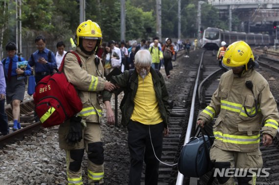 【홍콩=AP/뉴시스】홍콩에서 12일에도 격렬한 시위가 벌어지면서 곳곳에서 교통이 마비됐다. 사진은 한 노인이 운행중단된 기차에서 내려 선로를 걸어가면서 소방대원들의 부축을 받고 있는 모습. 2019.11.12