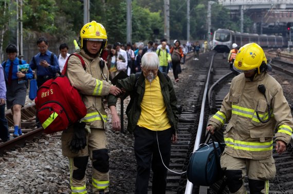 홍콩에서 12일에도 격렬한 시위가 벌어져 곳곳에서 교통이 마비된 가운데, 한 노인이 운행중단된 기차에서 내려 소방대원들 부축을 받으며 선로를 걸어가고 있다. AP 뉴시스