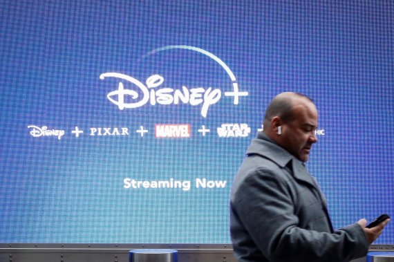 A man looks at his phone as he passes by a screen advertising Walt Disney's streaming service Disney+ in New York City, U.S., November 12, 2019. REUTERS/Brendan McDermid /REUTERS/뉴스1 /사진=