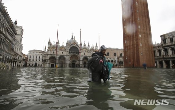 이탈리아 베네치아에서 12일(현지시간) 53년래 최악의 홍수가 발생해 산마르코 광장이 바닷물에 잠겨 있는 가운데 한 여성이 아이를 업고 물을 헤치며 걷고 있다. [사진=뉴시스]