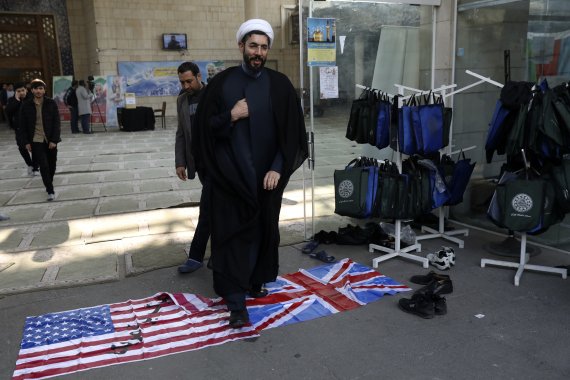 이란 수도 테헤란의 테헤란 대학 캠퍼스에서 14일(현지시간) 이슬람 성직자가 미국 및 영국 국기를 밟으며 지나가고 있다.AP뉴시스