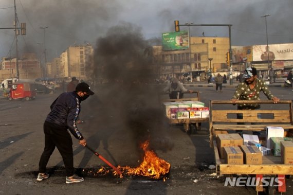 [바그다드=AP/뉴시스]지난 8일(현지시간) 이라크 수도 바그다드의 타흐리르 광장에서 이란의 미군 기지 미사일 공격에 항의하는 시위가 열려 한 남성이 도로를 봉쇄하기 위해 불을 지르고 있다. 이란은 이날 새벽 솔레이마니 사령관을 사살한 미국의 공습에 대한 보복으로 이라크 내 두 곳의 미군 기지에 미사일 공격을 감행했다. 2020.01.21