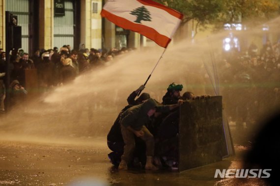 [베이루트=AP/뉴시스] 새로운 정부에 반대하는 레바논 반정부시위가 22일(현지시간) 베이루트 국회의사장 인근에서 시위 도중 물대포를 피하기 위해 나무 방패 뒤에 몸을 숨기고 있다.