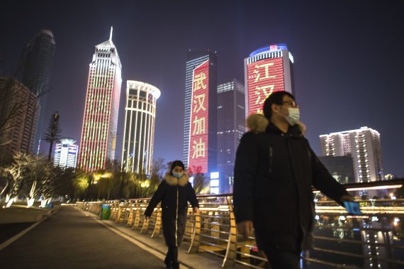 In this Friday, Jan. 31, 2020, photo released by China's Xinhua News Agency, people wearing face masks walk past buildings lit up with slogans of encouragement in Wuhan in central China's Hubei Province. (Xiao Yijiu/Xinhua via AP) /뉴시스/AP /사진=