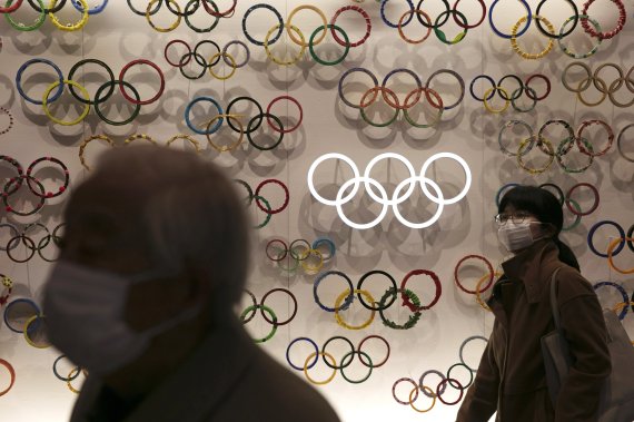 마스크를 낀 시민들이 일본 도쿄의 올림픽 박물관을 지나고 있다. 코로나19 확산 속도가 높아지는 가운데 국제올림픽위원회(IOC)가 오는 7월 일본에서 개최 예정인 도쿄올림픽의 취소 가능성을 제기했다. AP뉴시스