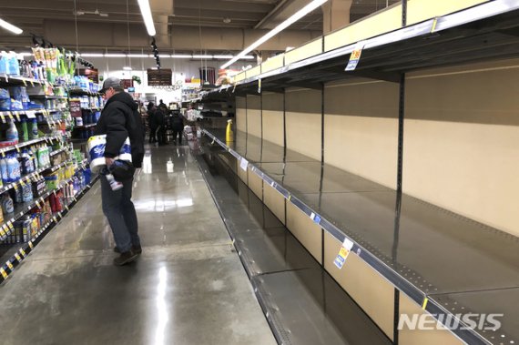 [시카고(미 일리노이주)=AP/뉴시스]미 일리노이주 시카고의 한 슈퍼마켓에서 지난 14일 화장지를 들고 있는 쇼핑객 1명이 텅 빈 식품 진열대 건너편의 청소용품들을 살펴보고 있다. 2020.3.15