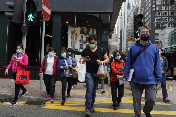 People wearing face masks walk on a street in Hong Kong Tuesday, March 17, 2020. For most, the coronavirus causes only mild or moderate symptoms, such as fever and cough. But for a few, especially older adults and people with existing health problems, it can cause more severe illnesses, including pn