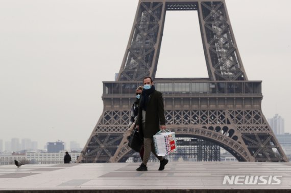[파리=AP/뉴시스]17일(현지시간) 프랑스 수도 파리에서 마스크를 쓴 남녀가 에펠탑 앞을 걸어가고 있다. 프랑스 정부는 신종 코로나바이러스 감염증(코로나19) 확산을 막기 위해 이날부터 이동제한령을 내렸다. 2020.3.18.