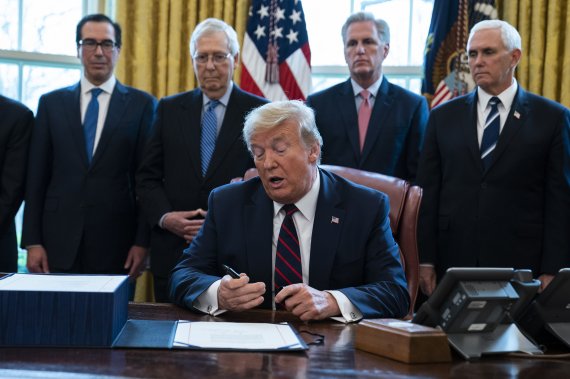 President Donald Trump opens a pen to sign the coronavirus stimulus relief package in the Oval Office at the White House, Friday, March 27, 2020, in Washington, as Treasury Secretary Steven Mnuchin, Senate Majority Leader Mitch McConnell, R-Ky., House Minority Leader Kevin McCarty, R-Calif., and Vic