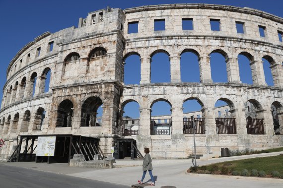 A jobless tourist guide walks past the first century AD Roman amphitheater that would be normally be crowded by tourists who are now absent because of the coronavirus outbreak, in Pula, Croatia, Sunday, April 5, 2020. (AP Photo/Darko Bandic) /뉴시스/AP /사진=