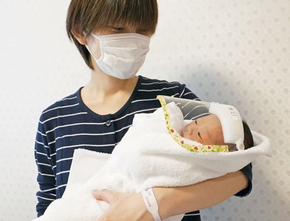 지난 5월 도쿄 인근 사이타마현의 한 병원에서 한 산모가 아기를 안고 있다. 코로나19 방역 조치의 일환으로 아기에게 투명 캡이 씌워져 있다. 로이터 뉴스1