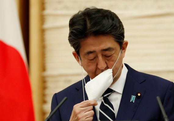 아베 총리가 지난달 25일 도쿄권 등에 대한 긴급사태 선언 해제와 관련한 기자회견을 하기 위해 마스크를 벗고 있다. 로이터 뉴스1
