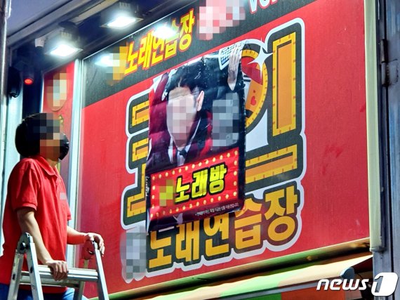 박원순 서울시장이 시내 모든 코인노래연습장(코인노래방) 집합금지 행정명령을 내린 지난달 22일 밤 서울 마포구 홍익대 앞의 한 코인노래연습장의 직원이 대형 사다리를 동원해 간판 위에 일반노래방(노래연습장) 포스터를 붙이면서 영업 재개를 꾀하고 있다./뉴스1 © News1 황덕현 기자