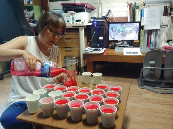 17일 밤 권대희씨 어머니 이나금씨가 자택에서 권씨가 수술 중 흘린 혈액과 안면윤곽수술의 평균 실혈량을 비교하기 위해 붉은 물감을 푼 물을 종이컵에 부어보이고 있다. 권씨가 수술 중 흘린 혈액 추정치인 3500cc(종이컵 약 20개)와 평균 실혈량 300cc(종이컵 2개)가 확연히 비교된다. 사진=김성호 기자