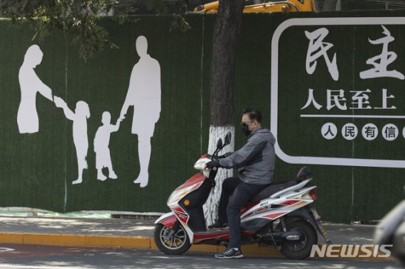 [베이징=AP/뉴시스]지난달 18일 중국 베이징 거리에서 마스크를 쓴 한 남성이 '민주주의' '국민 우선'이라는 정부 선전 문구가 적힌 벽화 앞에서 오토바이에 앉아 있다.