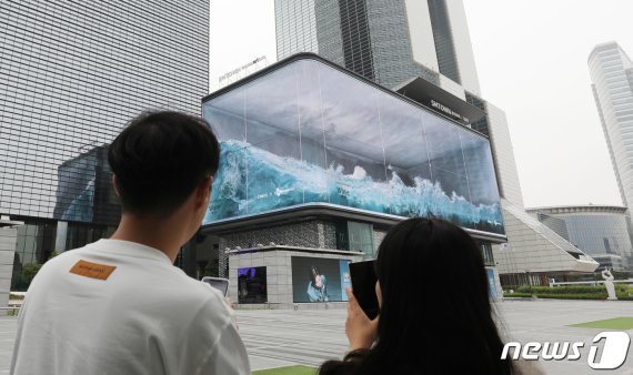 서울 강남구 삼성동 코엑스 앞 '파도(Wavw)'가 전 세계적인 관심을 끌며 한국의 초대형 실감콘텐츠 기술력이 조명받고 있다. 코엑스 앞을 지나던 시민이 전광판에서 몰아치는 디지털 파도를 스마트폰에 담고 있다. 2020.5.25/뉴스1 © News1 박지혜 기자