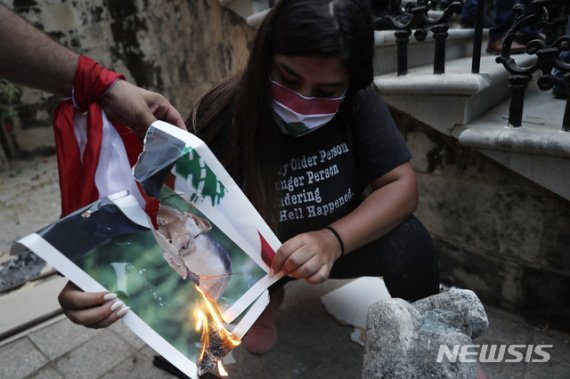 [베이루트=AP/뉴시스] 8일(현지시간) 레바논 수도 베이루트 외교부 건물 앞에서 열린 반 정부 시위에서 한 여성이 미셸 아운 대통령 사진을 불태우고 있다. 2020.08.09