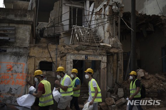 [베이루트=AP/뉴시스]13일(현지시간) 레바논 베이루트에서 자원 봉사자들이 지난주 폭발 참사로 훼손된 건물 앞으로 지나고 있다. 2020.8.14.