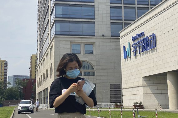 FILE - A woman uses her phone as she passes by the ByteDance headquarters in Beijing, China, on Friday, Aug. 7, 2020. The Chinese government is complicating the U.S.-government-ordered sale of U.S. TikTok assets. China on Friday, Aug. 28, 2020 introduced export restrictions on artificial intelligenc